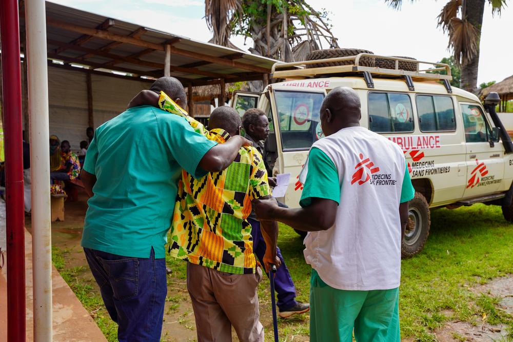 Deux membres du personnel médical de MSF aident un patient à atteindre la voiture ambulance de MSF à la clinique de Jansuk, dans le comté de Yei, en Equatoria central. © Manon Massiat/MSF