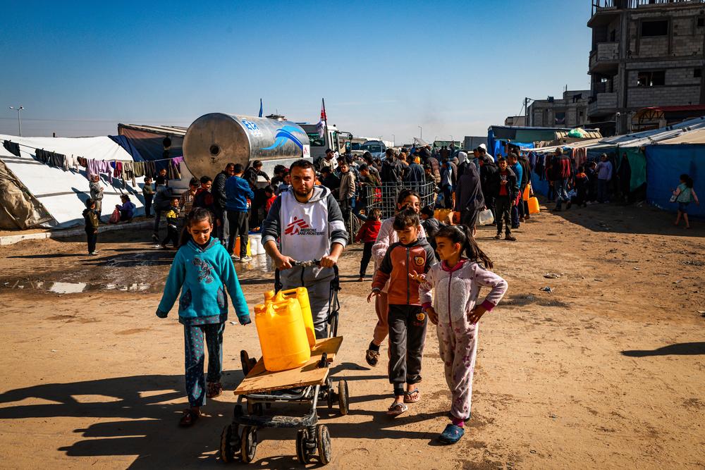 Youssef Al-Khishawi, un agent MSF chargé de l'eau et de l'assainissement, aide des enfants à transporter de l'eau jusqu'à leur tente dans le quartier de Tal Al-Sultan, dans la ville de Rafah, au sud de Gaza, 27 janvier 2024. ©Mohammed Abed