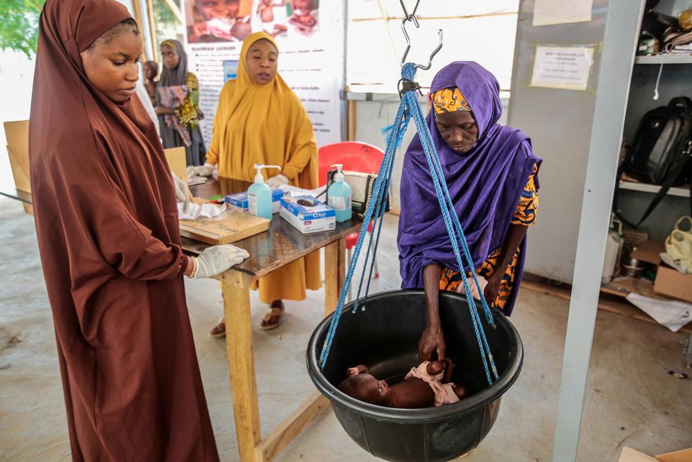 Des agents de santé évaluent le poids de l'enfant tandis que Fatima Isyaka place son enfant malnutri sur une balance au centre d'alimentation thérapeutique ambulatoire MSF de Kofar Marusa. État de Katsina, Nigeria, juin 2022.  © George Osodi