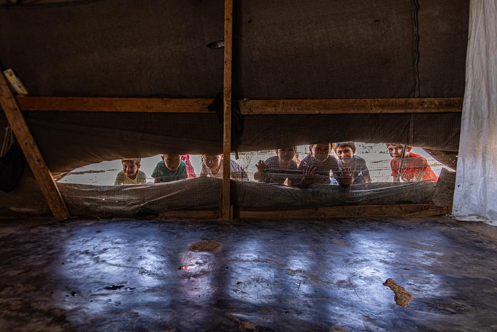 Des enfants réfugiés syriens regardent à travers l'ouverture de ventilation d'une tente. Juin, 2024 © Carmen Yahchouchi/MSF.