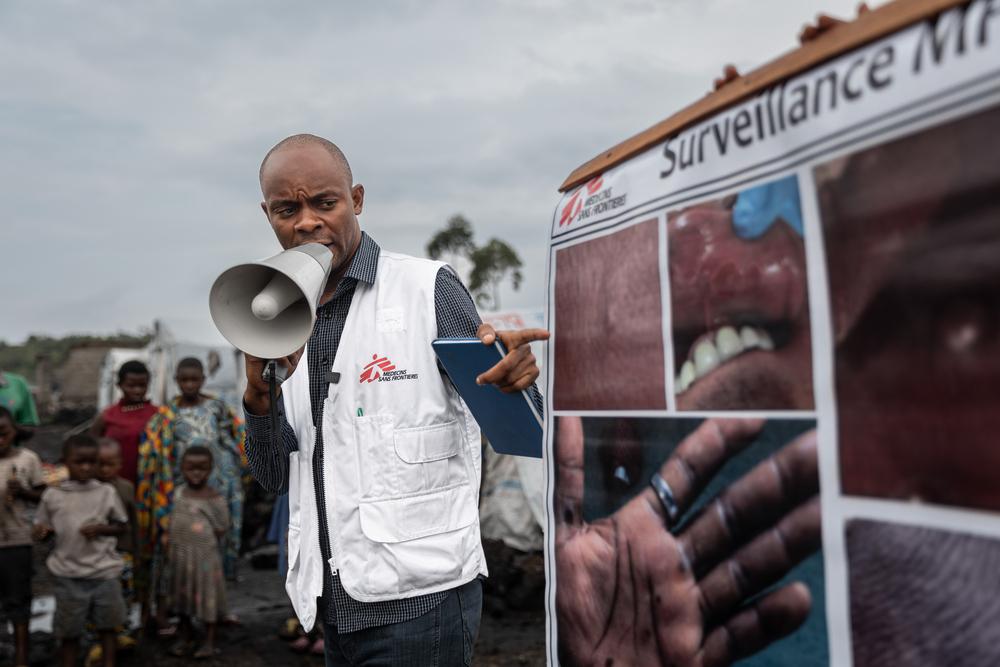 Le promoteur de la santé de MSF, Aristote Saidi Wanyama, utilise une affiche et un mégaphone pour diffuser des informations sur les stratégies de prévention de la mpox dans le camp de déplacés de Buhimba, à la périphérie de Goma