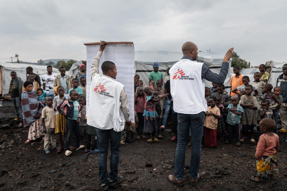 Les promoteurs de Santé de MSF utilisent un mégaphone et un poster pour diffuser des informations sur les stratégies de prévention de la mpox dans le camp de déplacés de Buhimba, à la périphérie de Goma