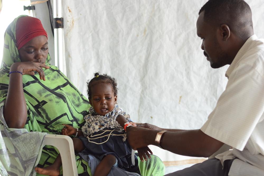 Latifa, 3 ans, est assise sur les genoux de sa mère à la clinique MSF du camp de Zamzam, au nord du Darfour, tandis qu'une infirmière effectue un dépistage MUAC pour vérifier sa santé nutritionnelle.