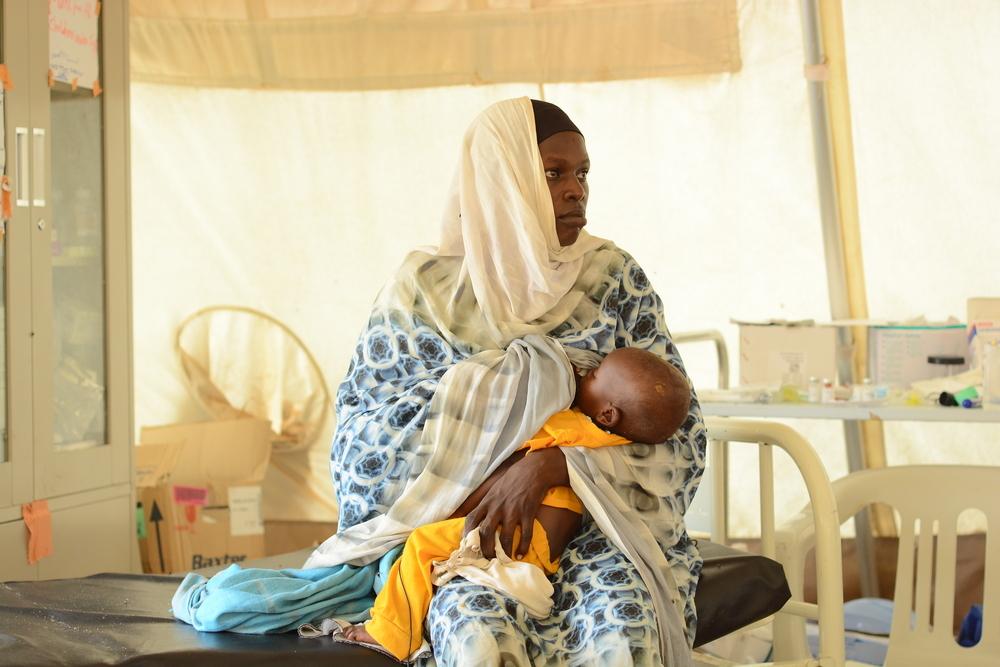 Saadiah, avec sa fille à la clinique MSF du camp de Zamzam, au Darfour du Nord, regarde une infirmière effectuer un dépistage PB pour évaluer la santé de son enfant.