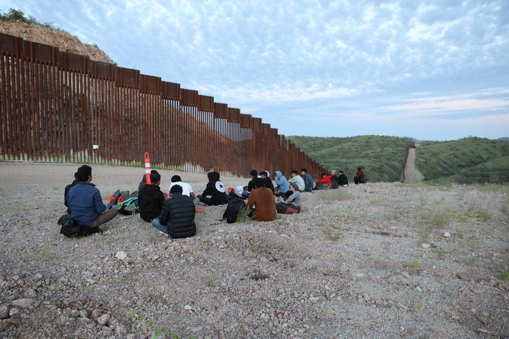 Des migrants et des demandeurs d'asile du Bangladesh et du Népal attendent que la police des frontières américaine vienne les chercher le long de la route non pavée à côté du mur frontalier entre les États-Unis et le Mexique à Sasabe, en Arizona. 