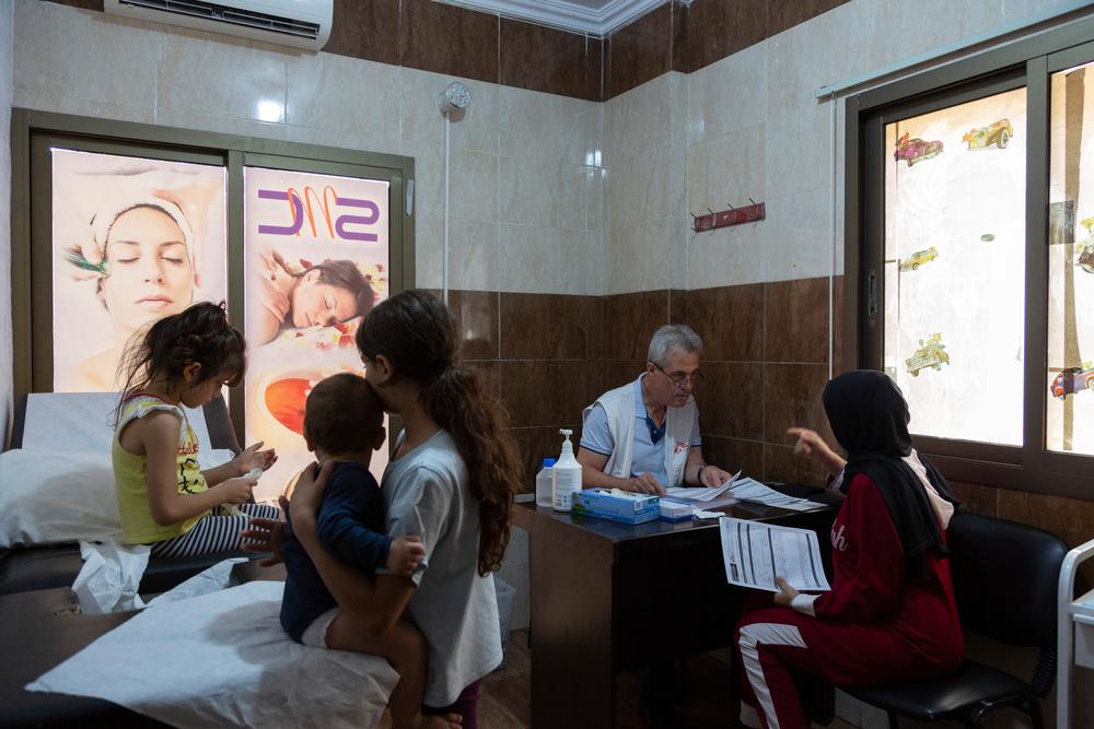 Le Dr Ali Daher, de MSF, prend des informations auprès de Najah pendant que ses enfants Maya, tenant Sary, 9 mois, et Lujain, 6 ans, l'attendent dans une clinique du centre de soins de santé primaires