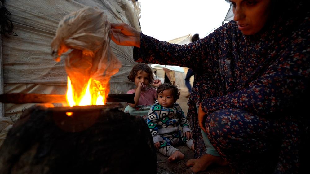 With no access to cooking gas, Yasmin is forced to light a fire using plastic to prepare a meal for her children, finding alternative ways to feed her family in dire conditions. 