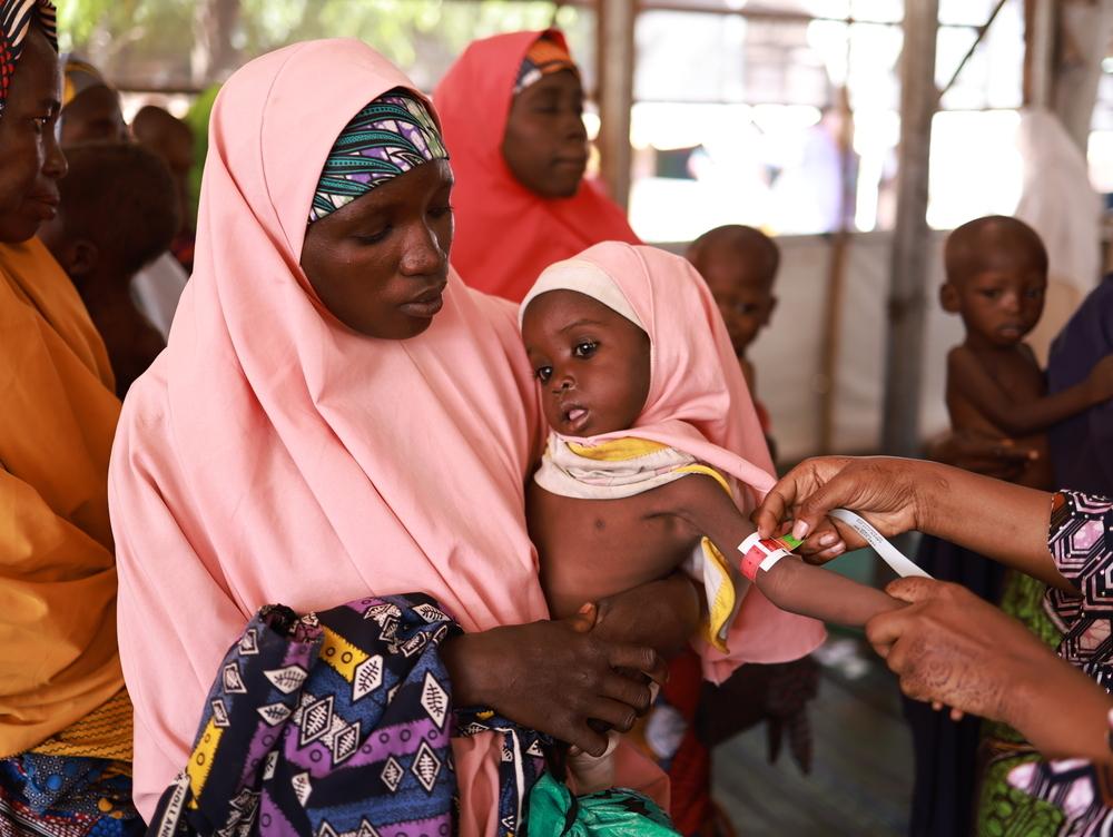 Na'ima, 25 ans, tient sa fille de 2 ans dans ses bras tandis qu'un membre du personnel de MSF mesure sa circonférence brachiale au centre d'alimentation thérapeutique ambulatoire Kofar Marusa, à Katsina, dans l'État de Katsina.