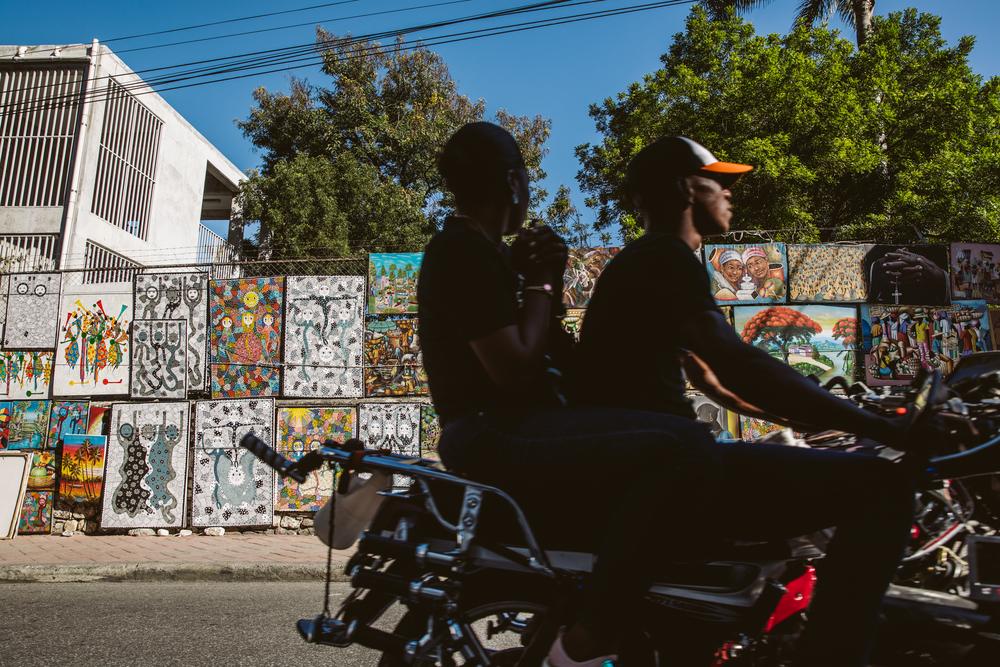 Un taxi-moto passe devant des peintures exposées dans une rue de Pétionville, à Port-au-Prince.