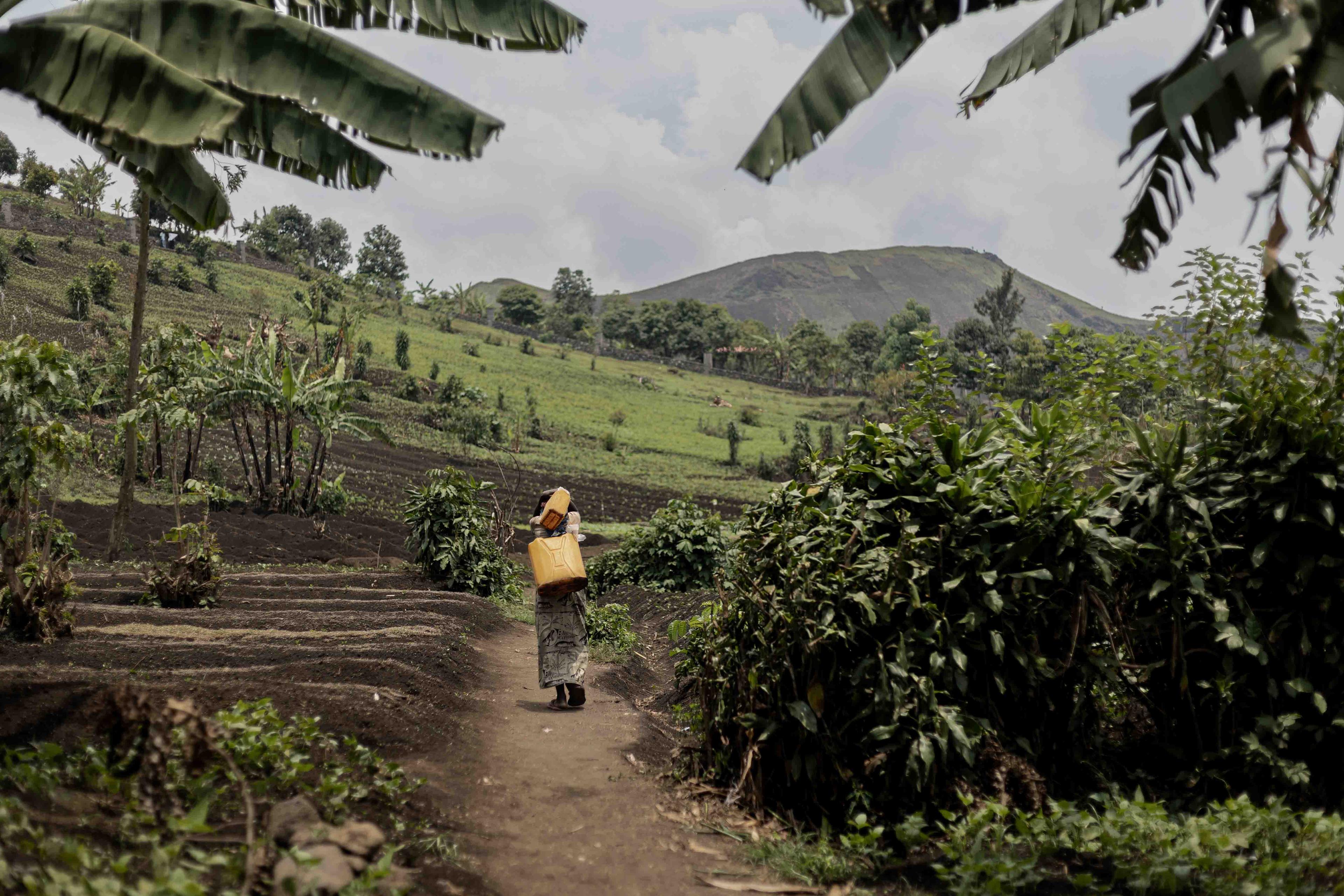 Une femme marche dans les montagnes avec un récipient d'eau sur le dos après l'avoir rempli à la station de distribution d'eau de MSF dans le camp de Sam Sam, à Goma, au Nord-Kivu, en RDC