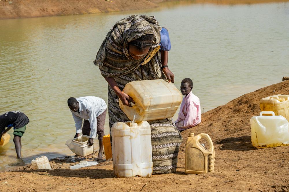 Des habitants du campement informel d'Atam récupèrent de l'eau dans un bassin à l'aide de jerricans. Les équipes de MSF travaillent au traitement de l'eau pour assurer l'approvisionnement en eau potable des personnes déplacées fuyant la guerre au Soudan.