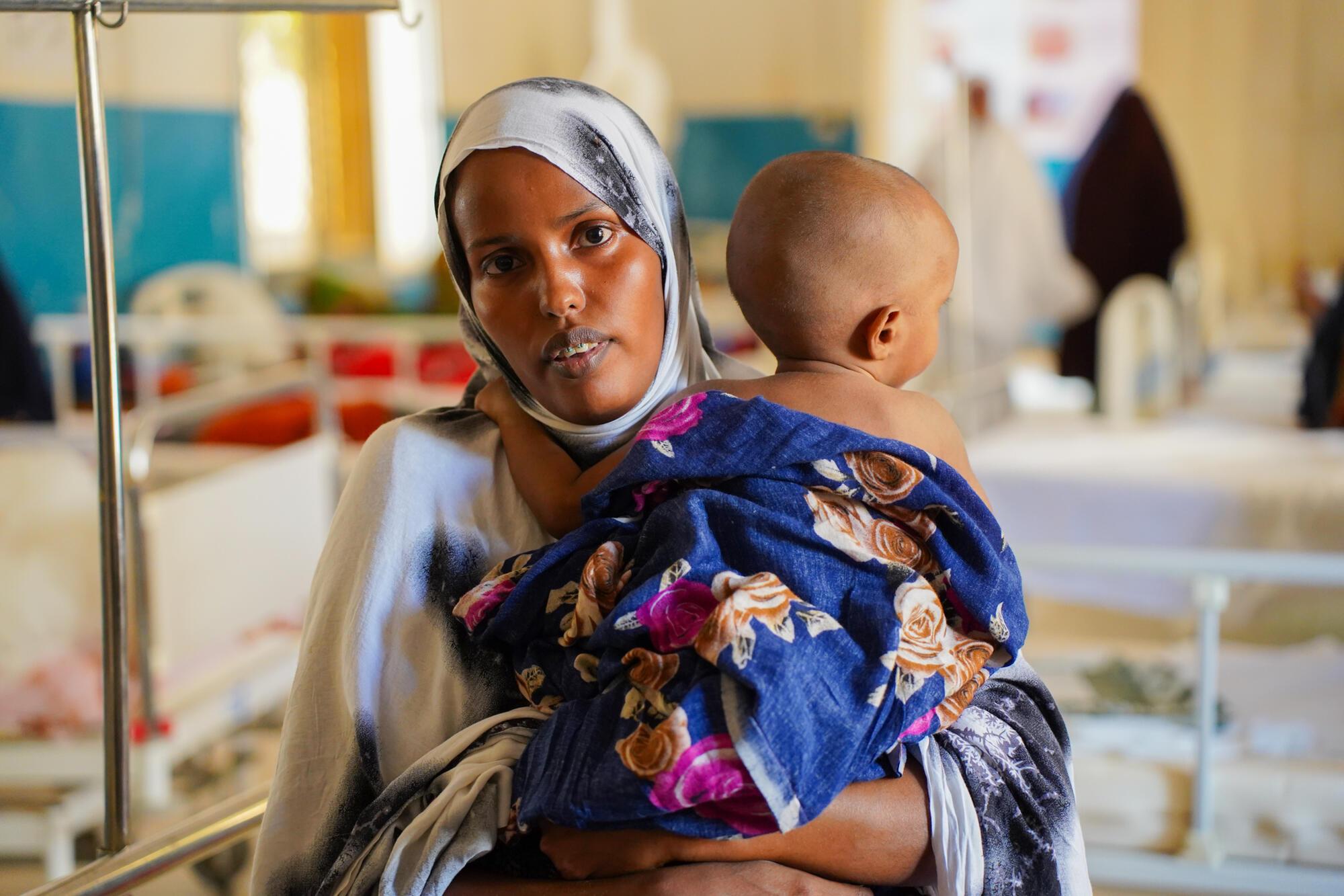 Suado Hassan Mohamed, 22 ans, tient son fils de 11 mois, Abdirahman Abdilatif, dans le service pédiatrique de l'hôpital régional de Bay, soutenu par MSF. Résidente de Baidoa, Suado a amené son fils pour qu'il soit soigné, car il est actuellement pris en charge pour malnutrition. Somalia, juin 2024 © Mohamed Ali Adan/MSF