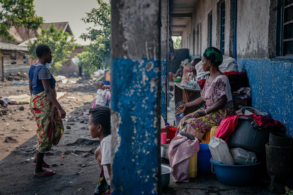 Des femmes, dont certaines sont victimes de violences sexuelles, et leurs enfants, sont assis à l’extérieur d’une école avec leurs matelas, vêtements et autres effets personnels. Ces familles se sont réfugiées dans l’établissement scolaire après avoir fui les violences. Elles doivent sortir leurs affaires chaque matin pour laisser la place aux élèves pendant les cours. Leurs maris, militaires, ont disparu lors de l’offensive des M23 sur la ville de Goma en janvier et février 2025. 