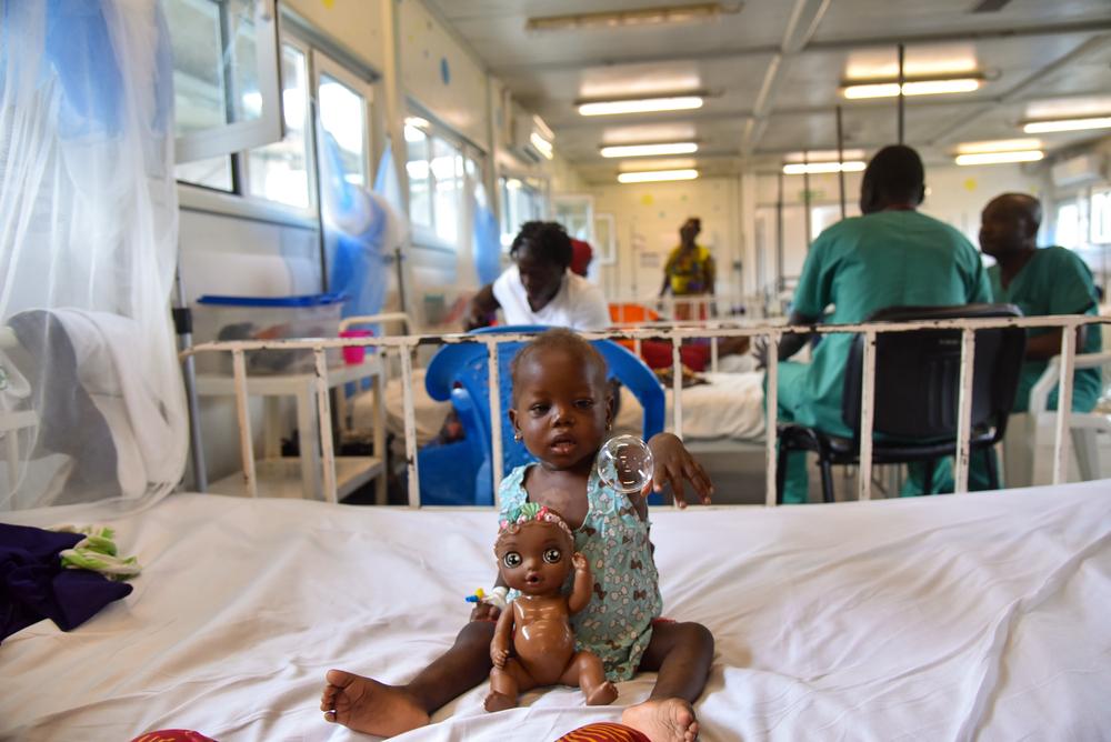 Maella Conteh, deux ans, est assise sur un lit et joue avec des bulles et une poupée à l'hôpital mère-enfant MSF à Kenema, en Sierra Leone