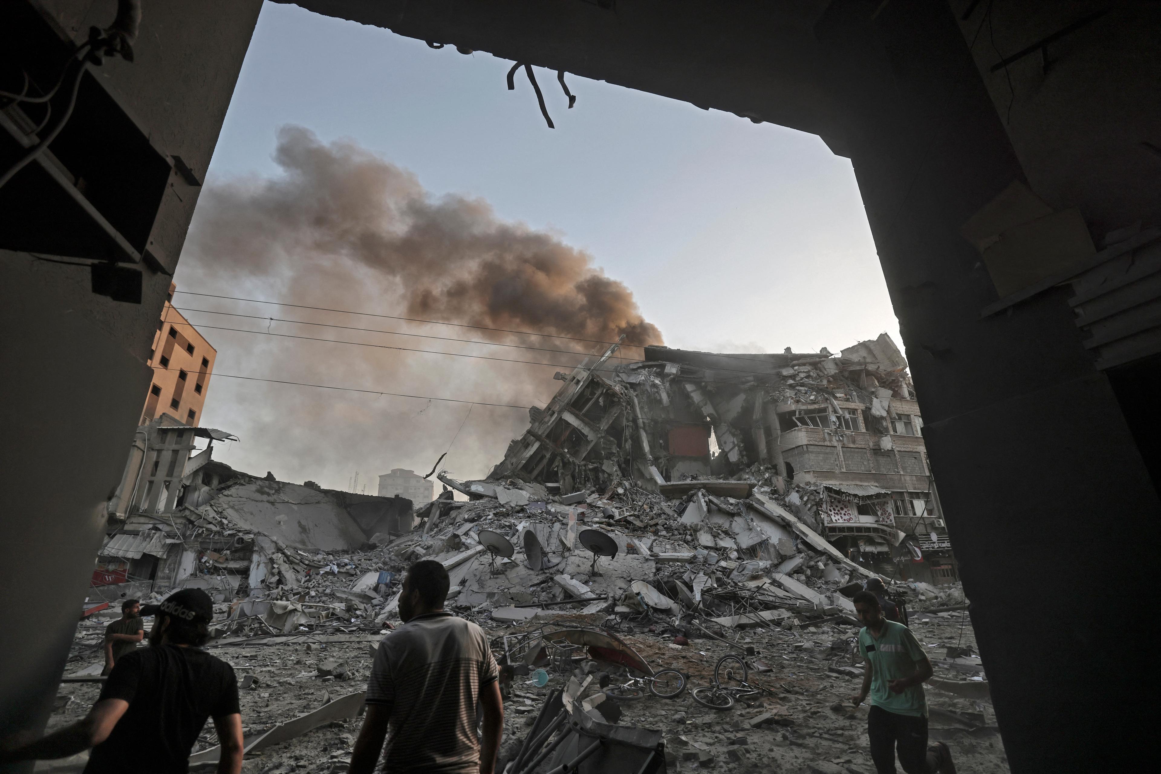 People gather amidst the rubble in front of Al-Sharouk tower that collapses after being hit by an Israeli air strike, in Gaza City, on May 12, 2021. 