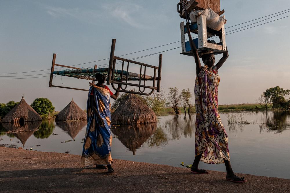 Women carry pieces of furniture and goods in a flooded area of Unity State. 