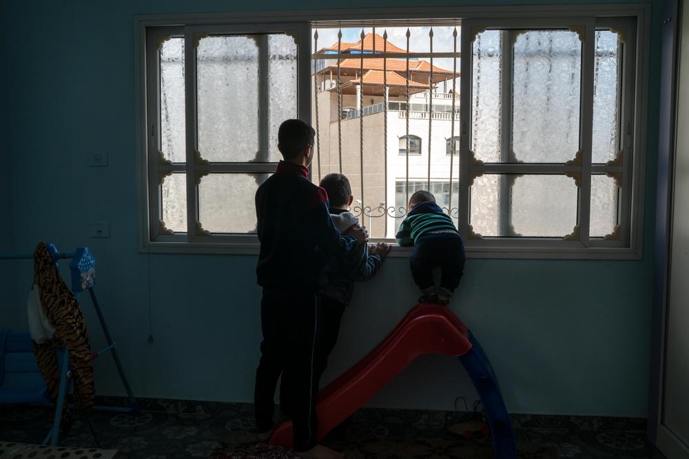 Hussam Odeh (G) et ses cousins regardent un soldat israélien à Huwwara de leur fenêtre le 13 avril 2023. 