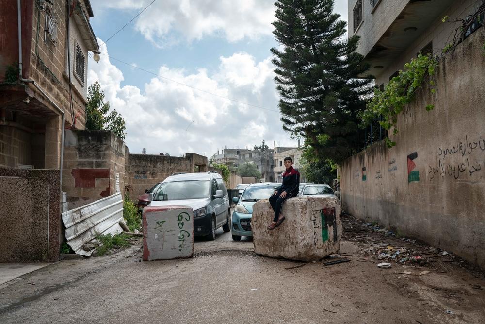 Hussam Odeh sits on a roadblock placed by Israeli soldiers in his neighborhood outside his home in Huwwara on 13 April 2023. 
