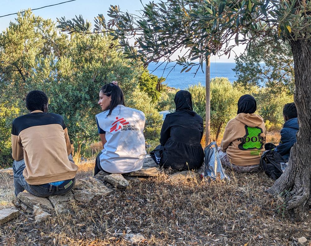 An MSF team member sits with a group of newly arrived people in Lesvos, who are resting after they have been assisted by MSF teams and provided with food and water. 