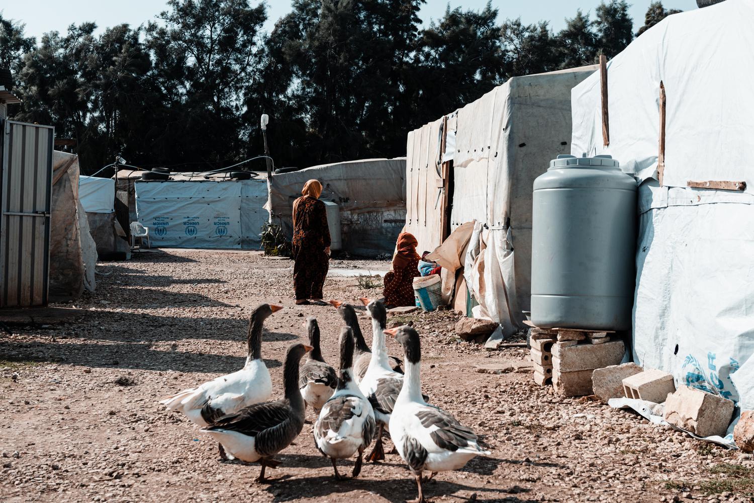 Two women talk in the middle of the informal tented settlement, lined with makeshift shelters, in Akkar governorate, near the Syrian border. Lebanon, December 2020. 