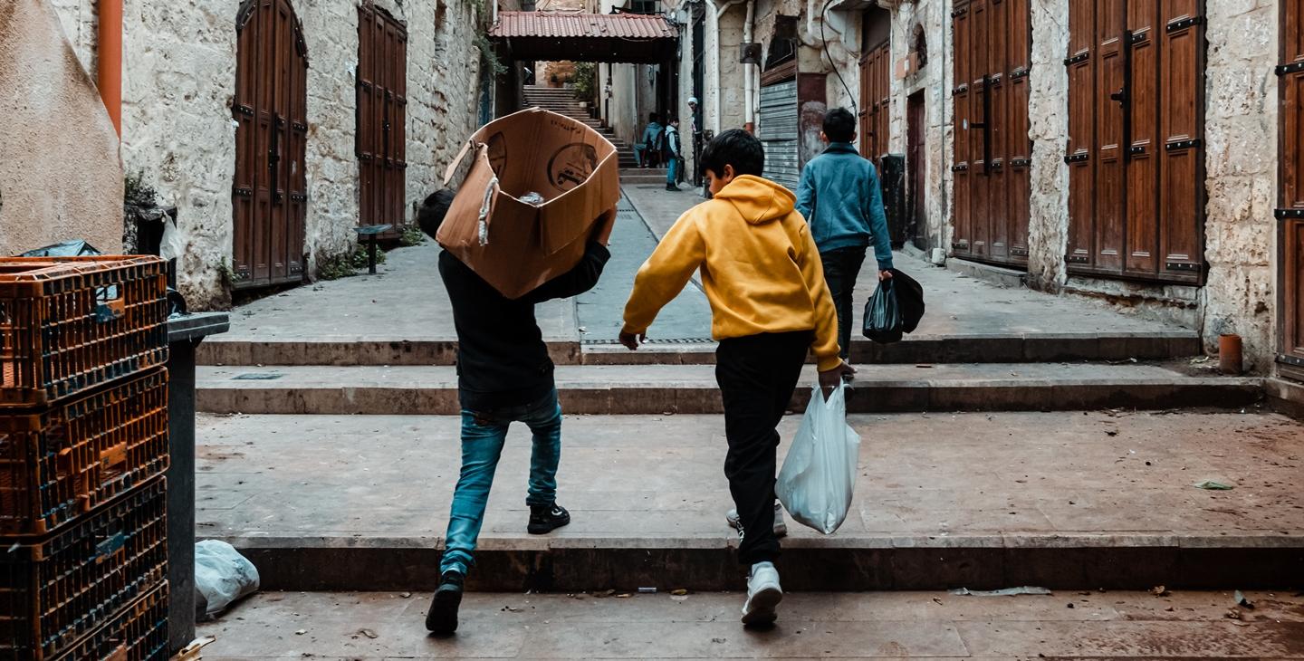 Children carrying goods in a rather empty street of the old souk in Tripoli. Lebanon, November 2020. 