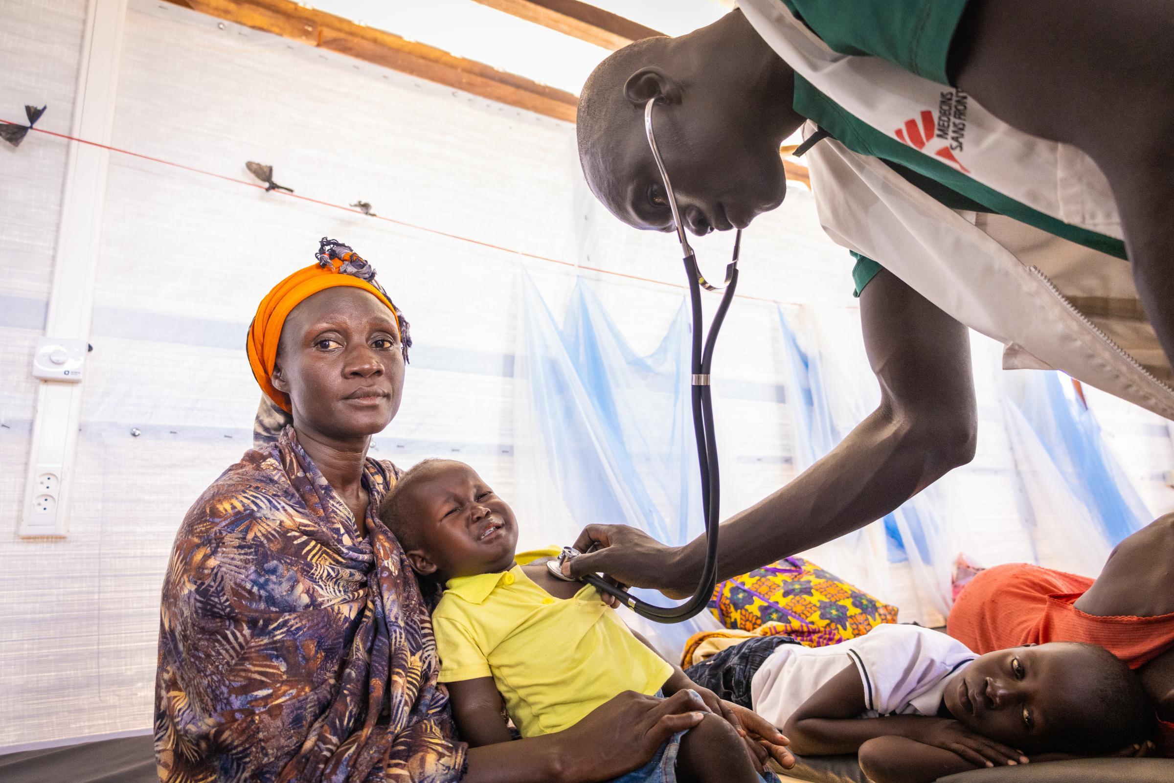 Une infirmière de MSF examine Atak Daniel, 2 ans, avec un stéthoscope pendant que sa mère le calme doucement dans le nouveau service de paludisme de l'hôpital d'État d'Aweil.