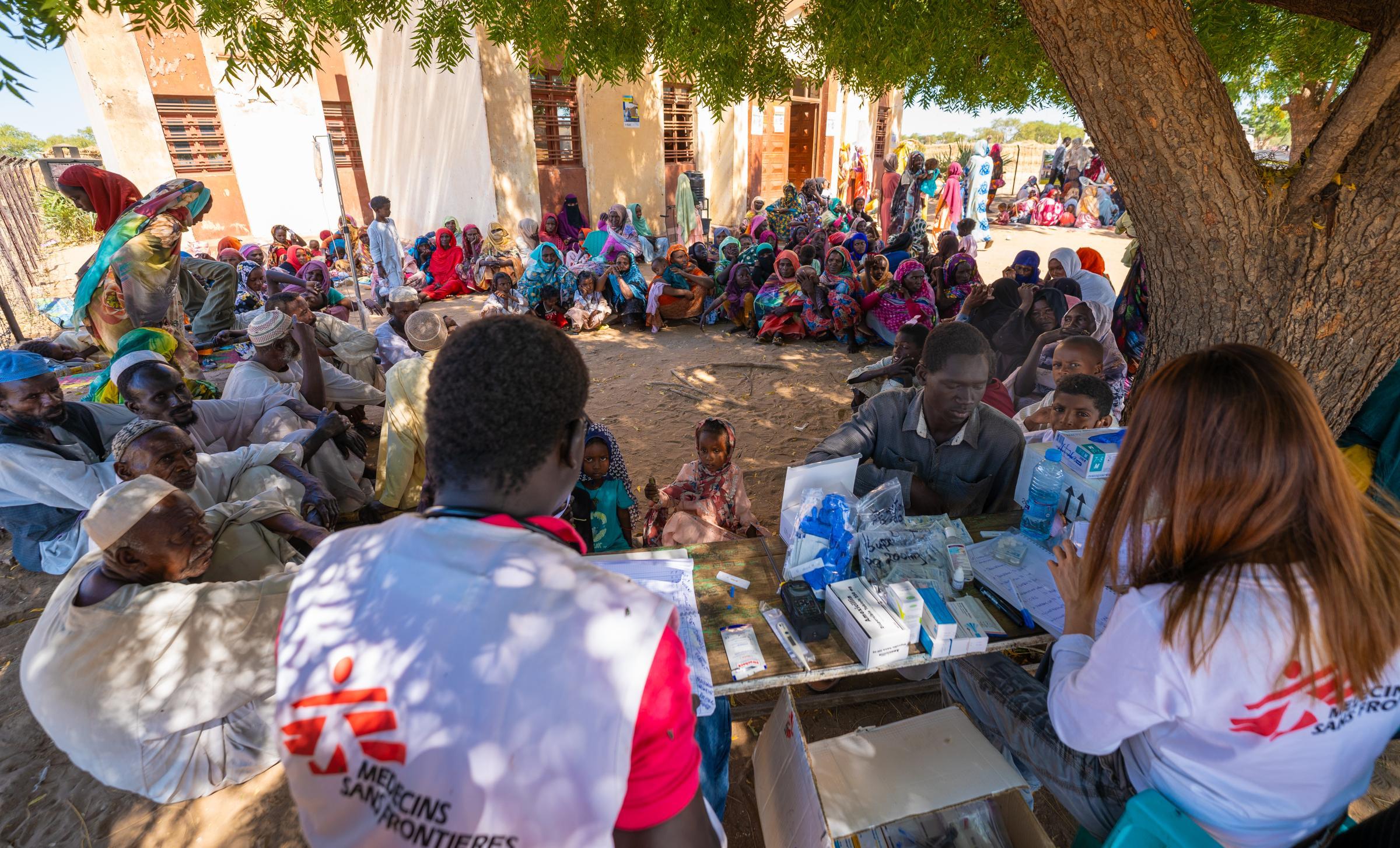 Une foule de rapatriés et de réfugiés fait la queue sous un arbre pour recevoir des soins de l'équipe de la clinique mobile MSF dans le campement informel de Jerbana.