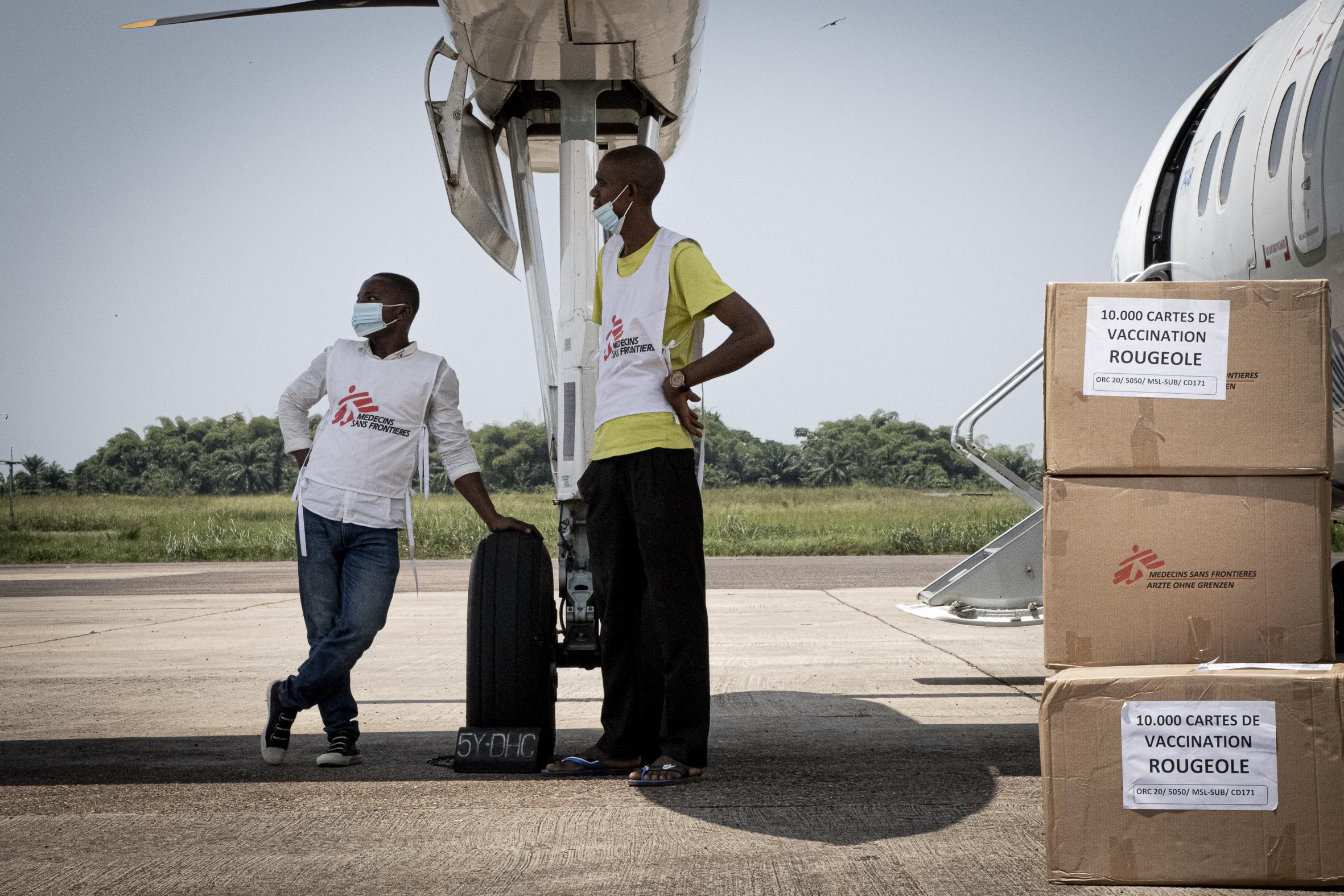 Les logisticiens de MSF, Losuka Platini et Bofiki Lucien, attendent près de l’avion pour commencer à charger les vaccins et autres kits médicaux dans les véhicules de MSF. Tarmac de l’aéroport international de Bangboka, à Kisangani, dans la province de la Tshopo. RDC, 2021 © Pacom Bagula/MSF