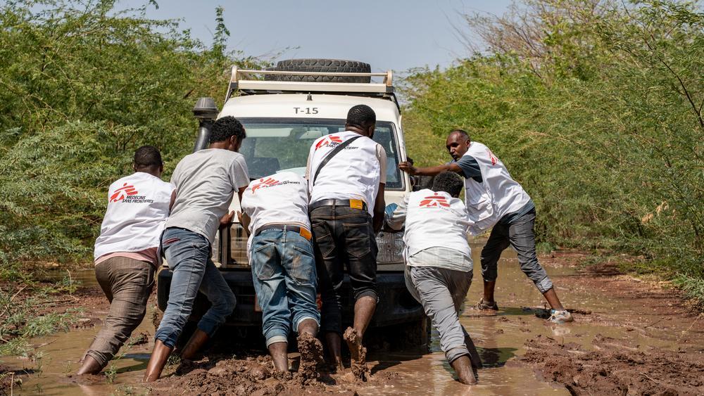 Des membres du personnel de MSF poussent un véhicule enlisé dans la boue à cause des chemins inondés, alors qu'ils se rendent dans l'un des centres de santé où MSF mène une campagne de sensibilisation, effectue des mesures du périmètre brachial et distribue des barres Plumpy'Nut aux enfants de moins de 5 ans. Ethiopie, novembre 2025 © Paula Casado Aguirregabiria/MSF