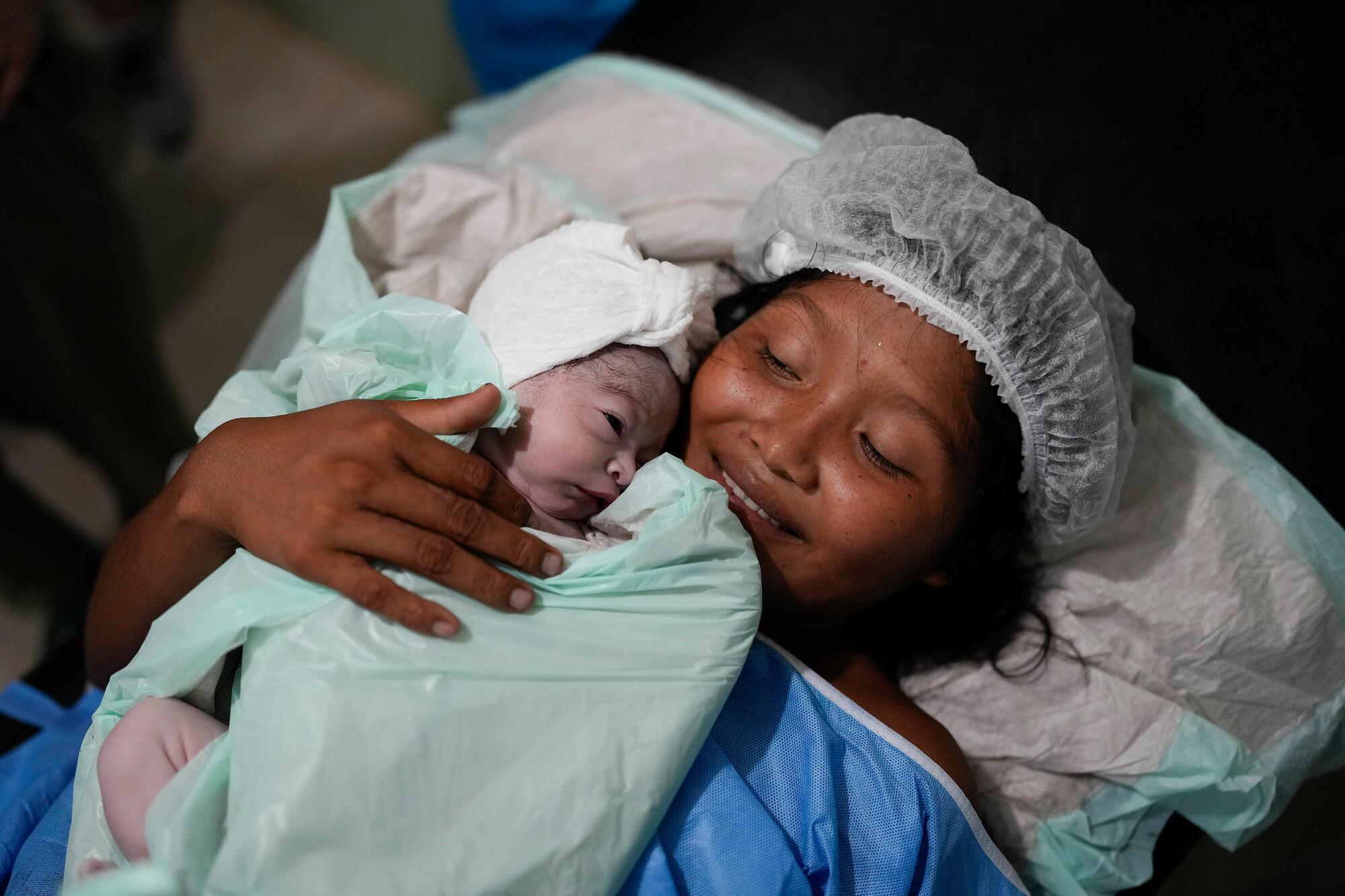 Adelia sourit en tenant son fils José Antonio sur ses genoux. À 18 ans et après des heures de travail, elle se sent épuisée, mais avec la joie de tenir son nouveau-né dans ses bras. Delta Amacuro, au nord-est du Venezuela. Mai, 2023 © Matias Delacroix