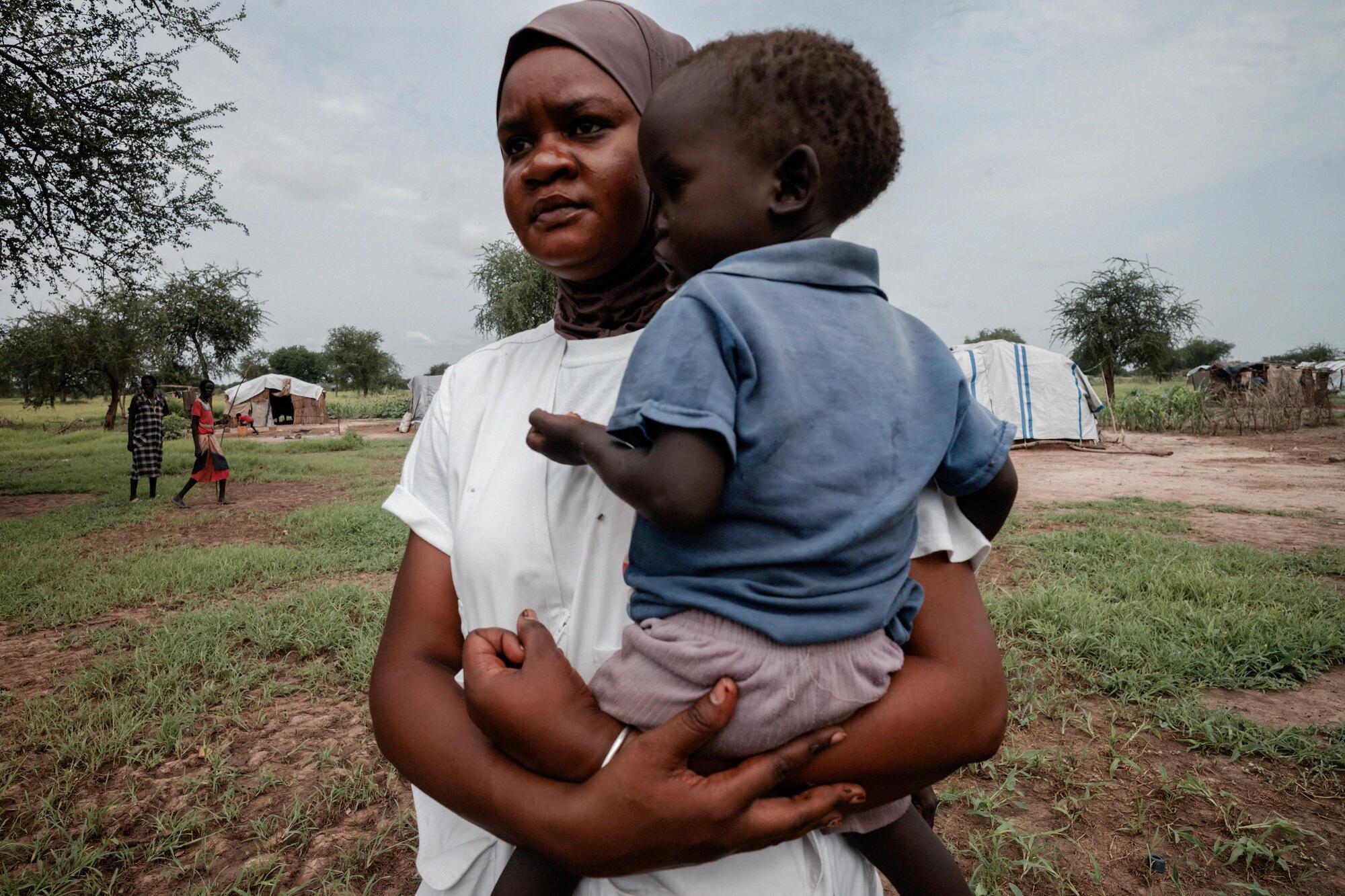 Awa Abdumadou, chef d'équipe de la gestion intégrée des cas communautaires (ICCM), aide à porter un enfant malade jusqu'au véhicule avant de le transporter avec sa mère à l'hôpital. © Sean Sutton/Panos Pictures