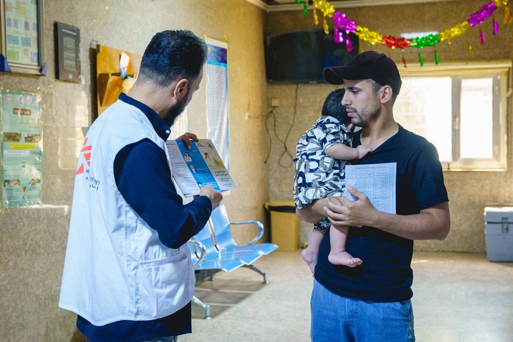 Un agent de santé de MSF s'entretient avec un père portant son enfant au centre de santé Mustafa Al-Adhari à Sadr City, Bagdad