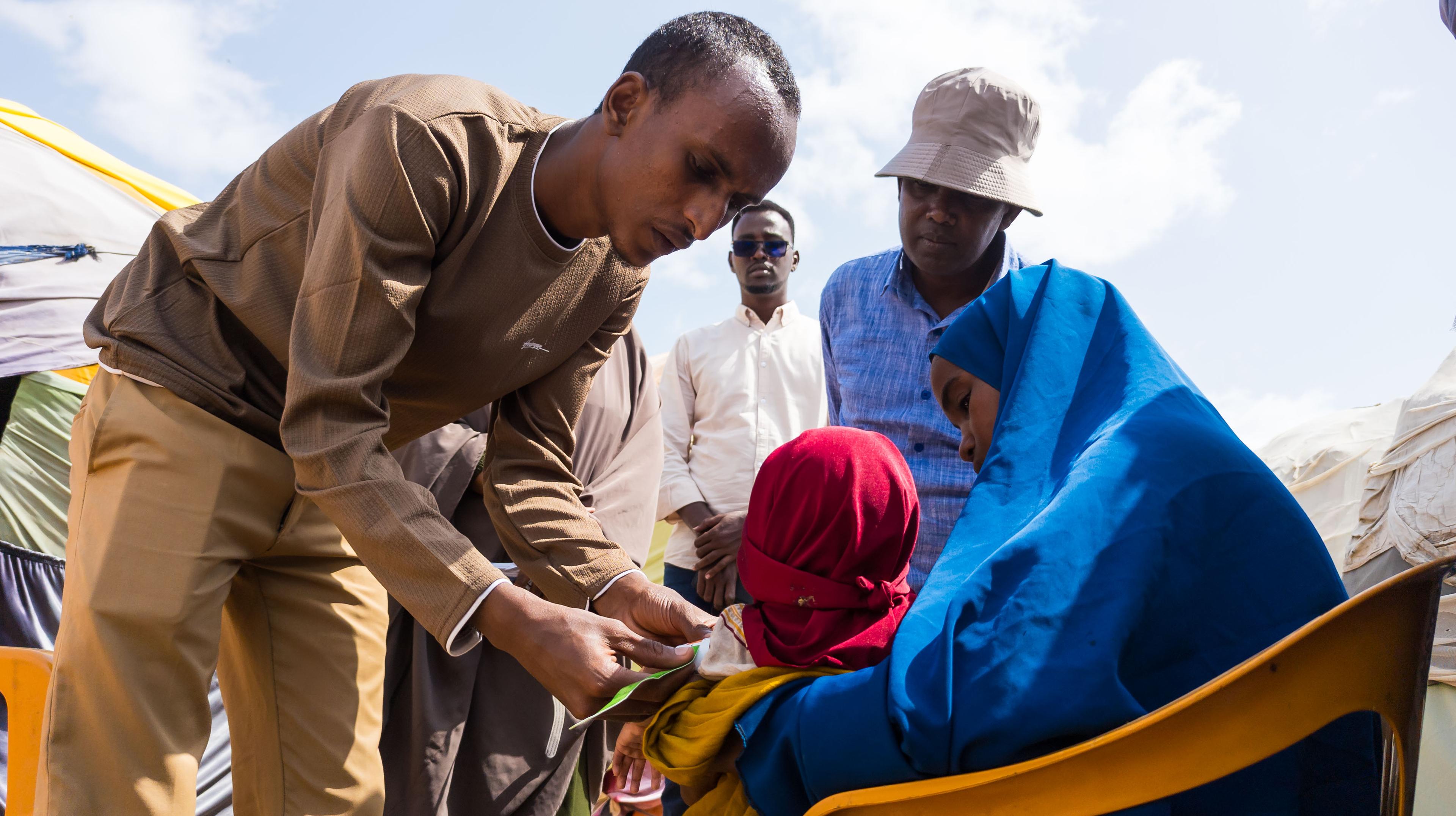 Mohamud Moktar, agent de santé communautaire, mesure le périmètre du bras à mi-hauteur (MUAC) d'un enfant dans un camp de personnes déplacées à Baidoa, en Somalie. Juillet, 2026 © Yahya Mohammed/MSF
