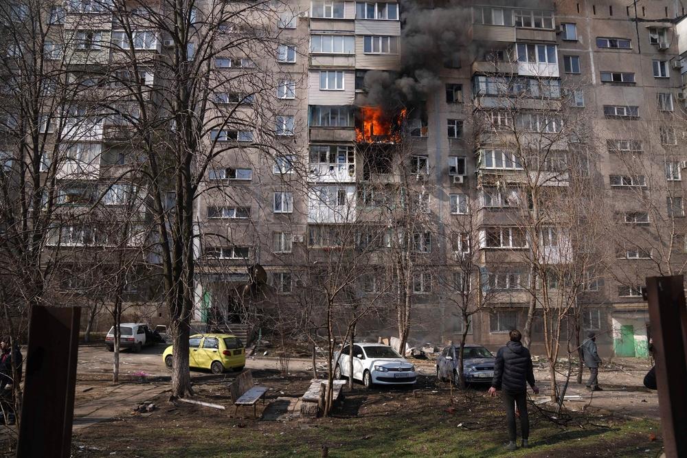 Des personnes regardent un immeuble d&#039;habitation en feu dans une cour après un bombardement à Mariupol, en Ukraine, dimanche 13 mars 2022. 