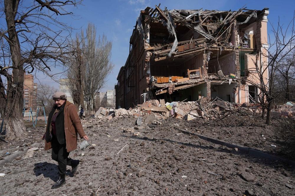 Une femme passe devant un bâtiment endommagé par un bombardement à Mariupol, en Ukraine, dimanche 13 mars 2022. 