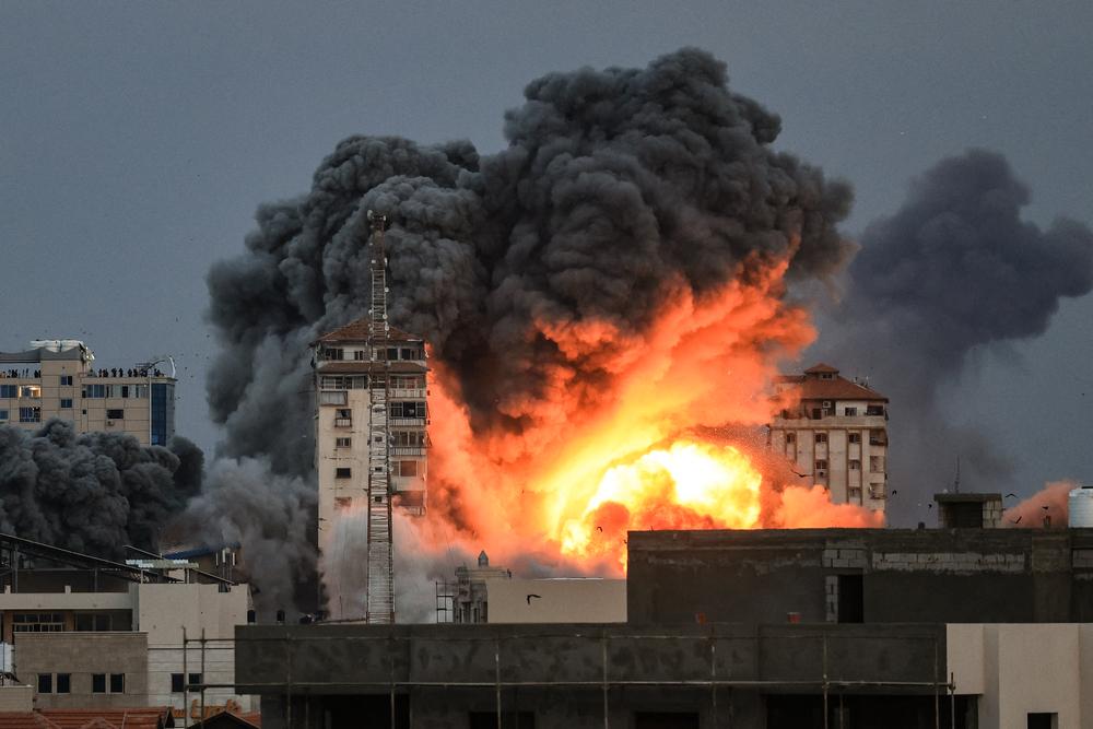 Des personnes se trouvant sur un toit regardent une boule de feu et de fumée s&#039;élever au-dessus d&#039;un immeuble dans la ville de Gaza le 7 octobre 2023 lors d&#039;une frappe aérienne israélienne qui a touché l&#039;immeuble Palestine Tower. 