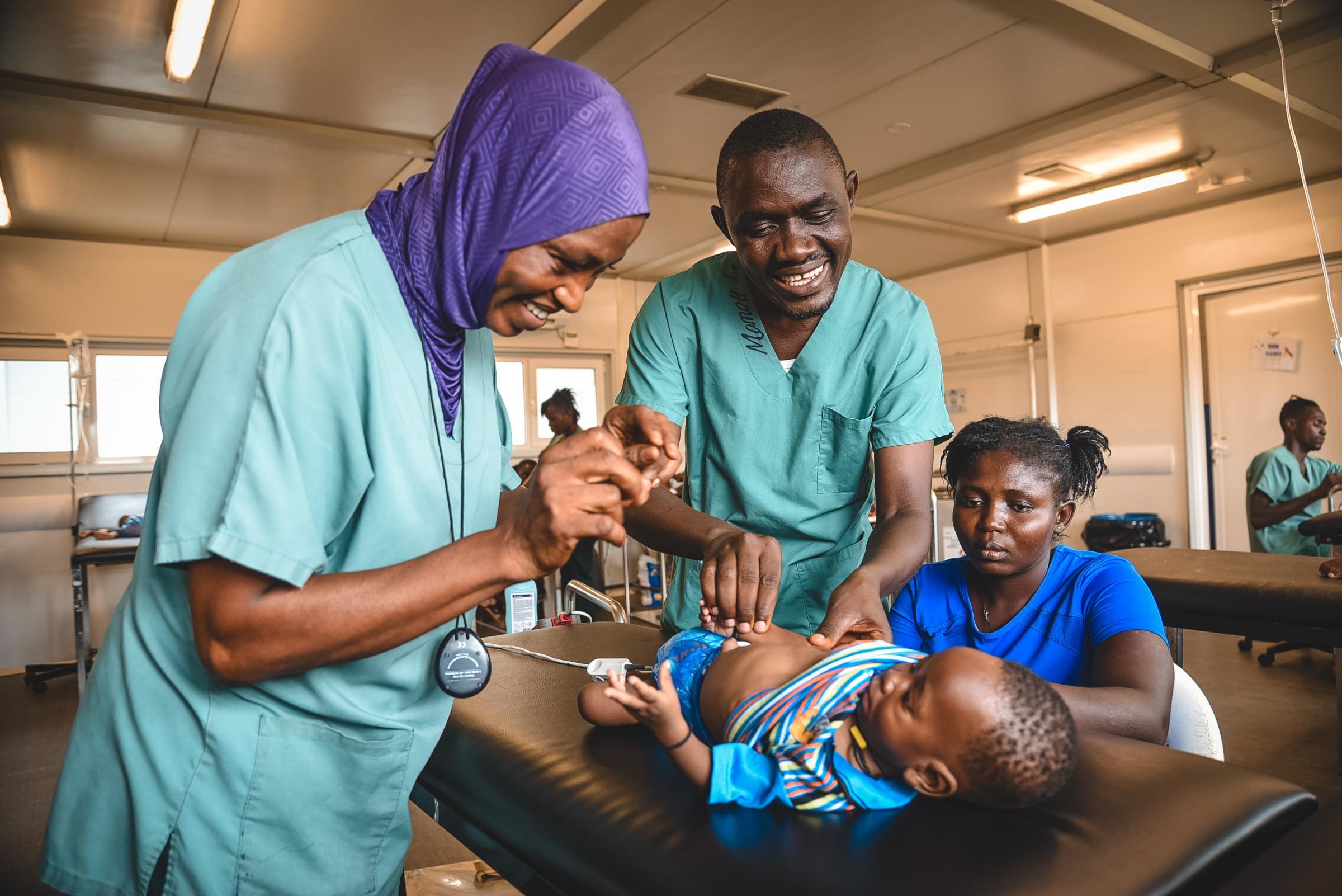 Momoh Sao, mentor clinique, et Aminata Koroma, aide-soignante, examinent Ogar Boima, 6 mois, aux urgences de l'hôpital mère-enfant MSF du district de Kenema, en Sierra Leone.