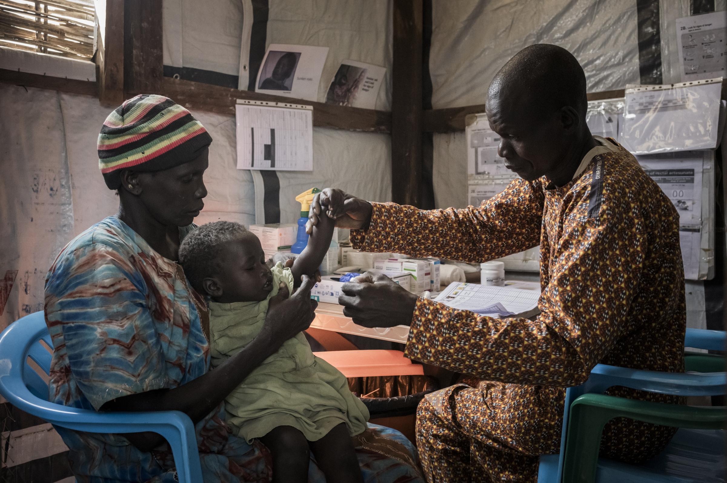 Dans la cabane de consultation pour la prise en charge communautaire intégrée, Mam Bol, 38 ans, membre de la communauté formée par MSF, effectue un test rapide de dépistage du paludisme sur Achuel Dutm, trois ans, tandis que sa mère, Aguak Dong, la soutient doucement. Mayen Abun, Soudan du Sud.