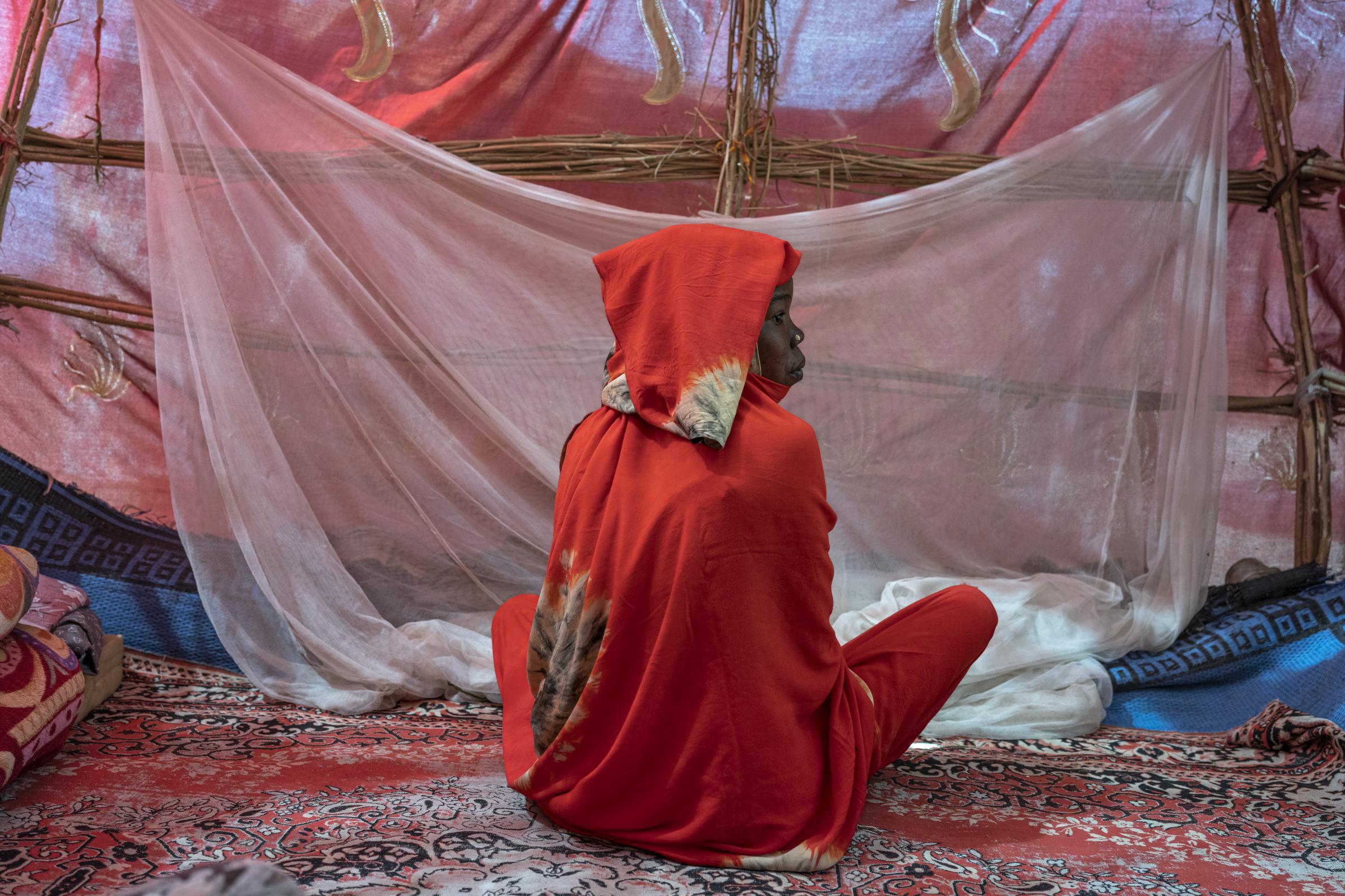 Fatima Djidda, dix-neuf ans, se trouve dans sa tente qu'elle partage avec sa sœur et ses neuf enfants. Devant elle, une moustiquaire qu'elle utilise la nuit pour se protéger des moustiques. N'Djamena, Tchad.