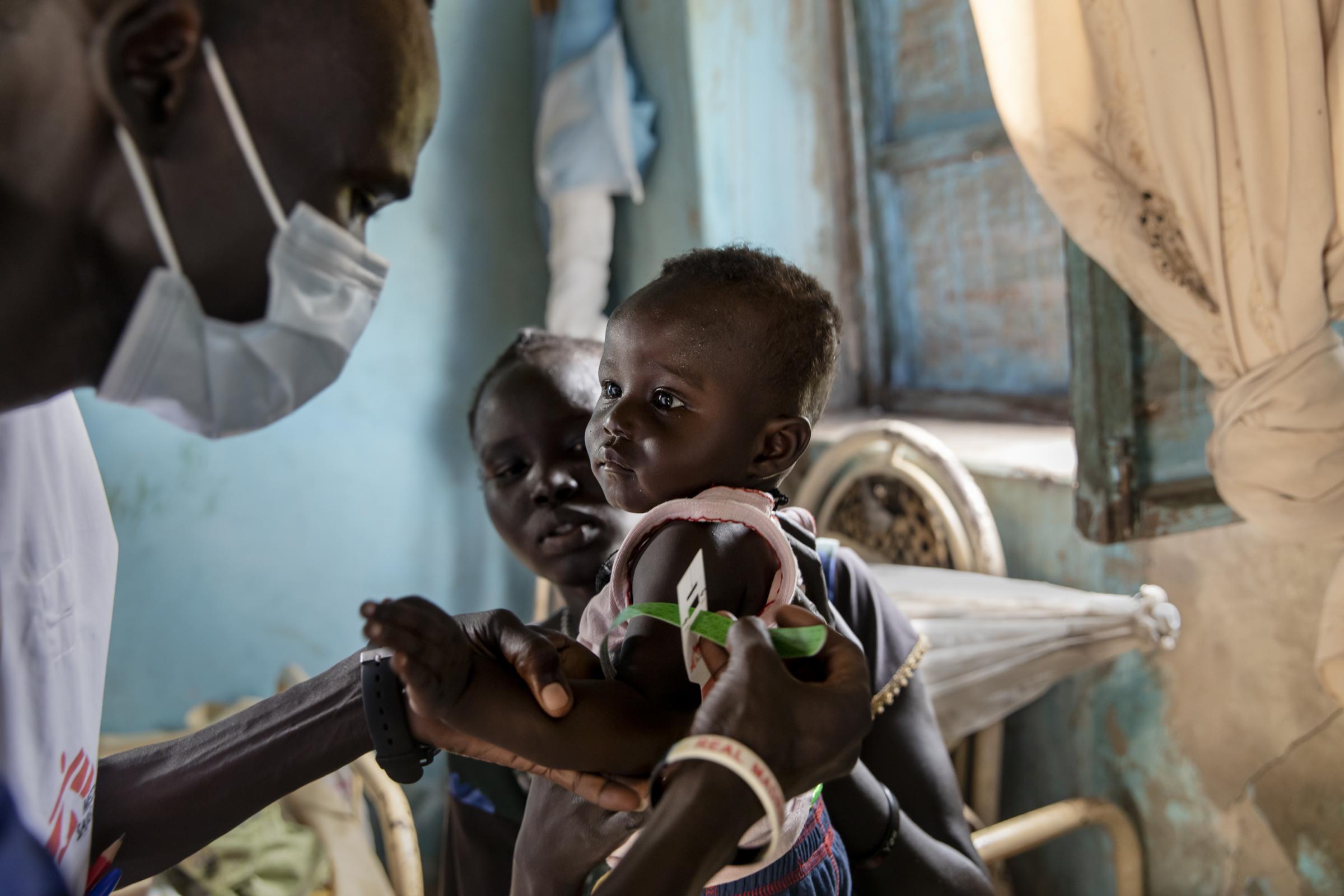 Ajok Atak tient son bébé Yel dans ses bras tandis qu'un membre du personnel de MSF mesure le niveau de nutrition de l'enfant dans sa maison près du village de Kuom, au Soudan du Sud