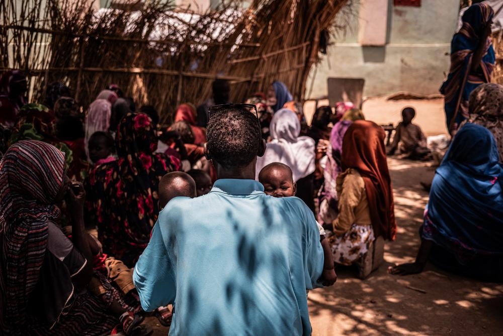 « Je n'ai pas de travail pour lui donner à manger. Nous sommes affaiblis. » Mohammed Khamis tient ses deux enfants dans ses bras lors d'un entretien avec l'équipe d'engagement communautaire de MSF, dans l'école transformée en camp de déplacés où ils vivent. Zalingei, Soudan, juillet, 2026 © Tadeu Andre/MSF