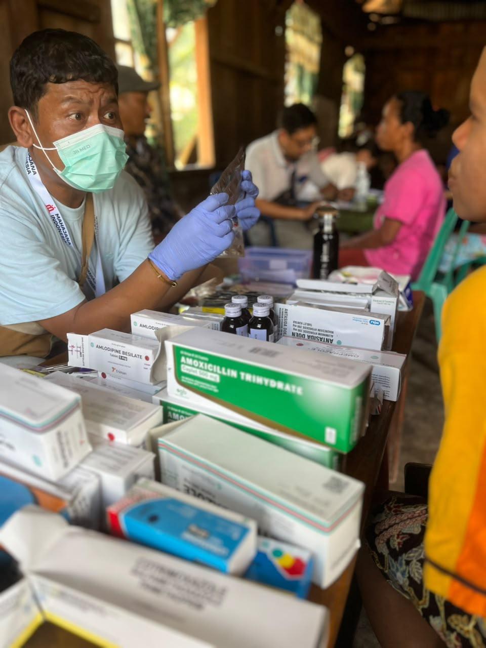 Un membre de l'équipe médicale de YMSFI explique un traitement à un patient lors d'une clinique mobile dans le district de Cibal Ouest, Indonésie
