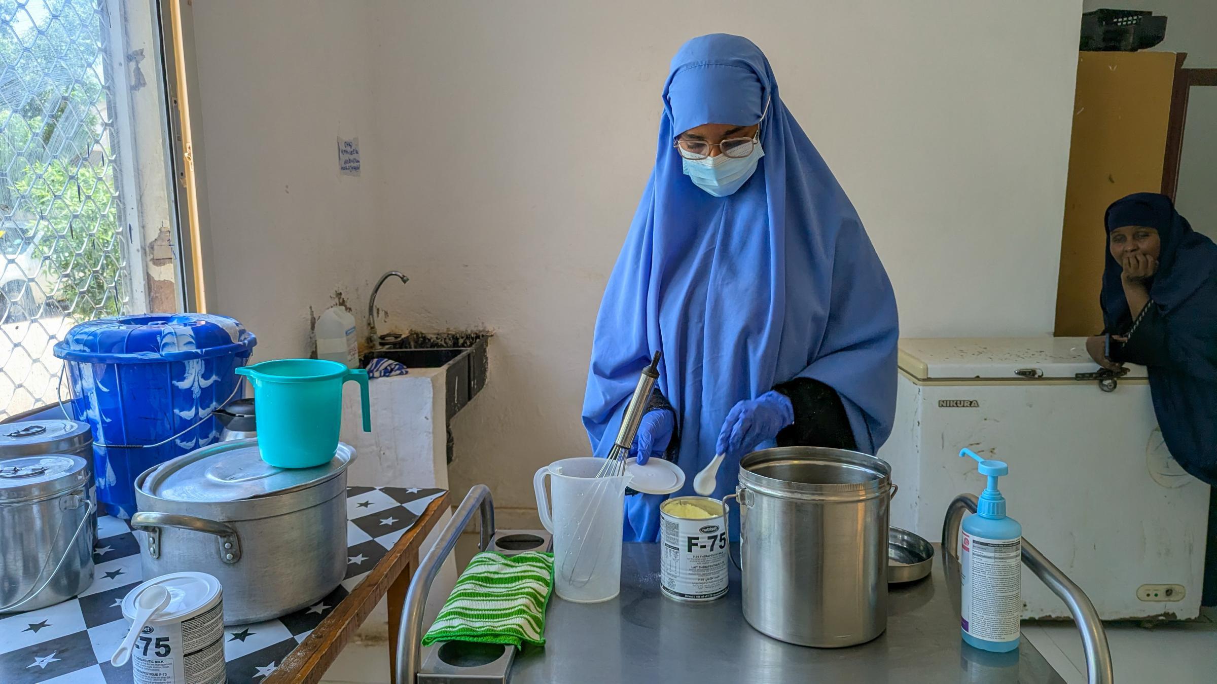 Dans la salle de préparation des repas du service de malnutrition de l'hôpital régional de Mudug, une infirmière prépare du lait thérapeutique F-75. Ce lait est utilisé en première phase de traitement, car l'organisme d'un enfant gravement malnutri ne tolère pas encore la formule plus énergétique administrée pendant la convalescence.