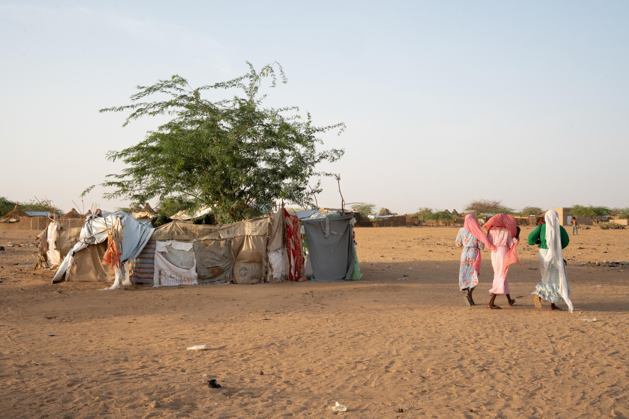 Des femmes passent devant des abris de fortune construits avec du carton, des sacs, du tissu et des bâches en plastique dans le camp de réfugiés de Ouré-Cassoni, Tchad