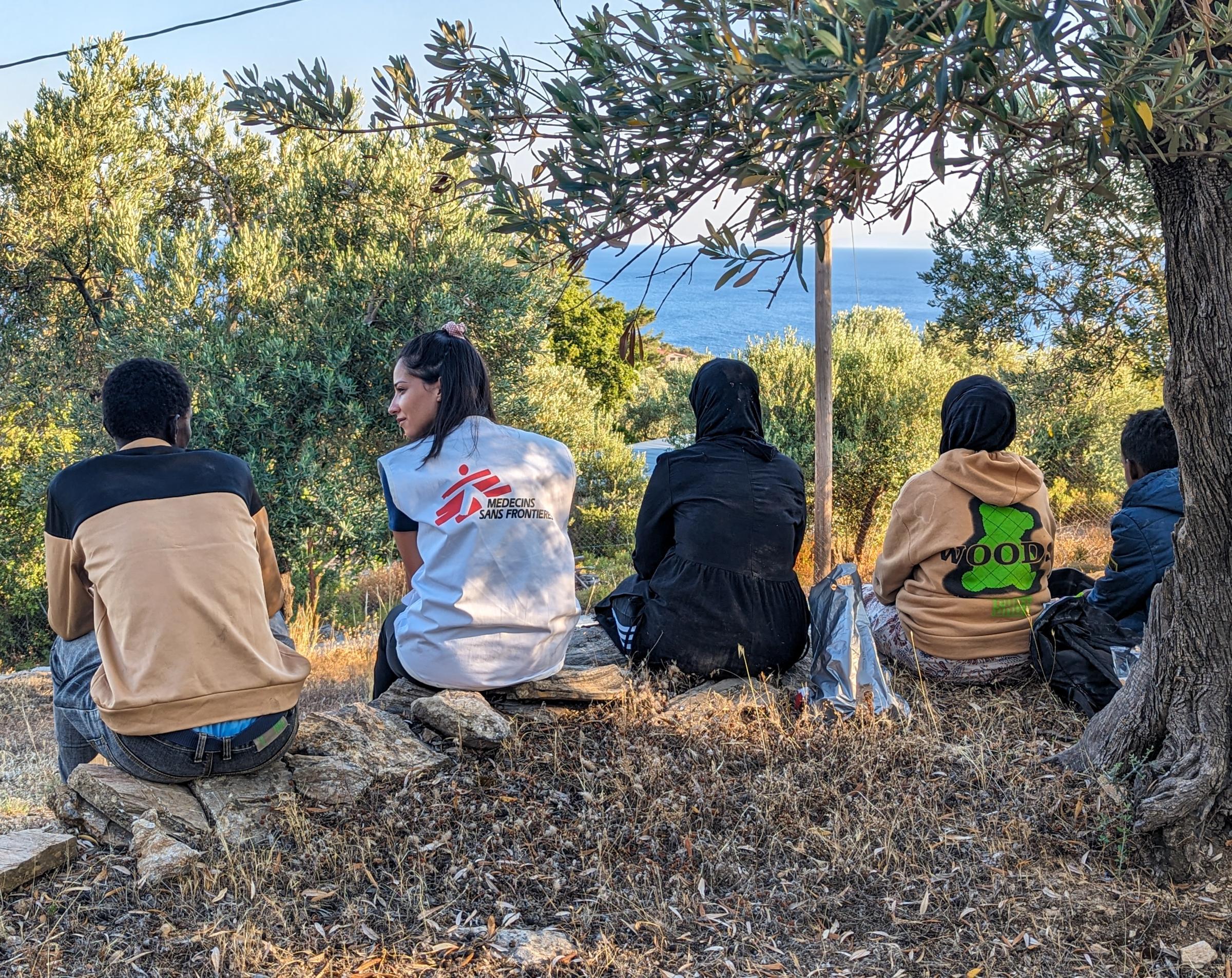 Un membre d'une équipe MSF est assis avec un groupe de personnes récemment arrivées à Lesbos, Grèce. Ces dernières se reposent après avoir reçu l'aide des équipes MSF et avoir reçu de la nourriture et de l'eau.